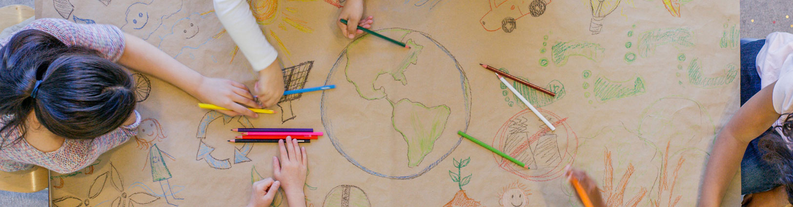 Children drawing with colored pencils on large piece of kraft paper